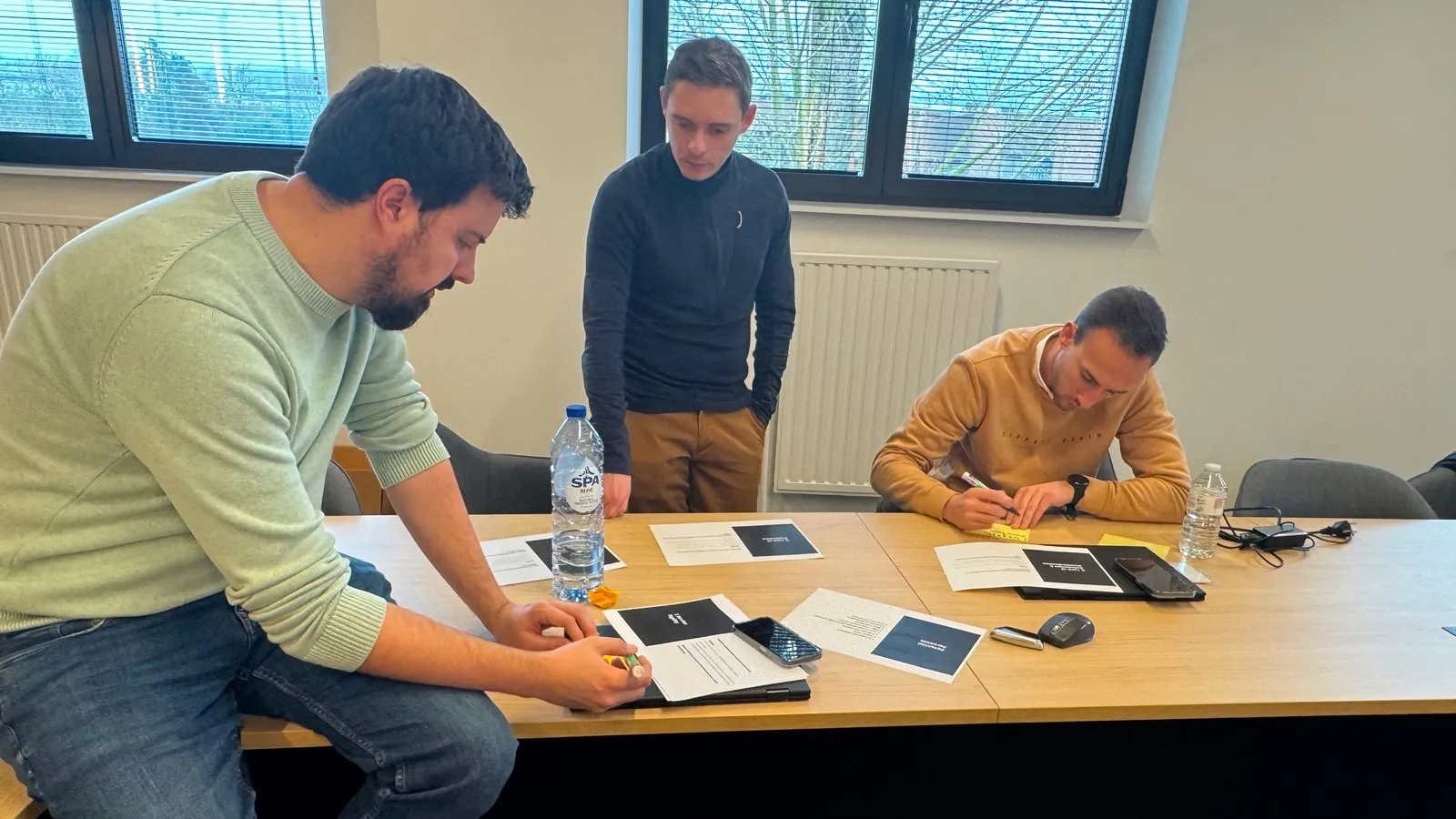 Drie deelnemers werken aan de tafel, kaarten en documenten van de workshop voor hen.